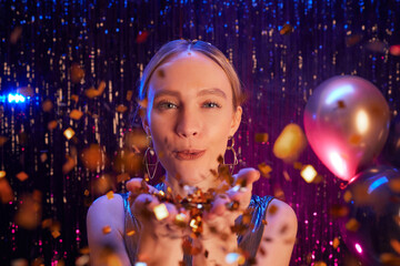 Close up portrait of beautiful blonde woman blowing glitter at camera while enjoying party in...