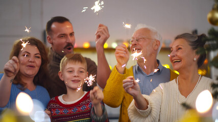 Cheerful family with different ages holding sparkles celebrating christmas - obrazy, fototapety, plakaty