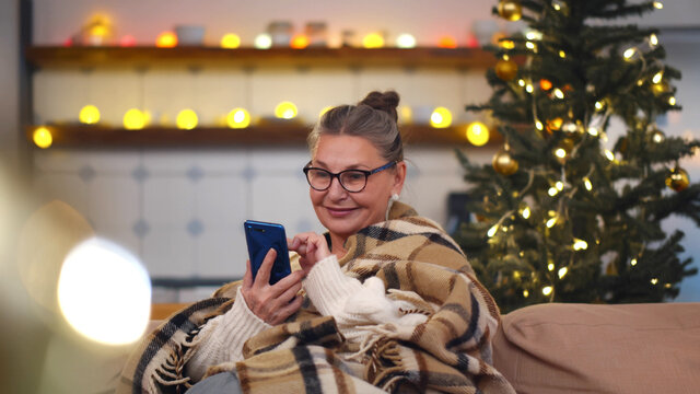 Senior woman sitting on sofa with smartphone at christmas time