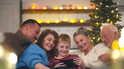 Happy family gathered on couch together using tablet watching christmas photos