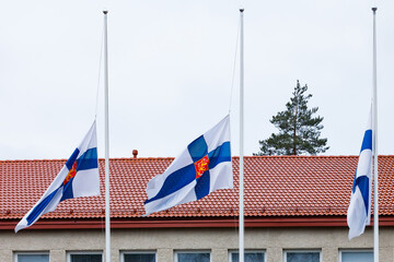 Three finnish flags lowered to half mast on the occasion of mourning at cloudy autumn day