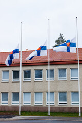 Fototapeta na wymiar Three finnish flags lowered to half mast on the occasion of mourning at cloudy autumn day