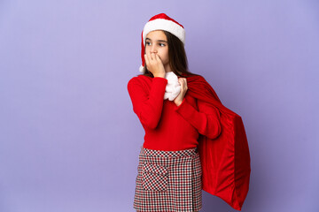 Little girl with hat and Christmas sack isolated on purple background having doubts