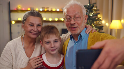 Senior couple with preteen grandson waving hands having video call on christmas eve