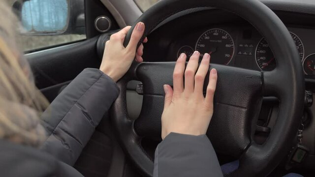 Close-up of a woman's hand pushing the horn on the steering wheel while driving.
