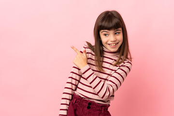 Little girl isolated on pink background surprised and pointing side