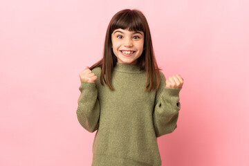 Little girl isolated on pink background celebrating a victory in winner position
