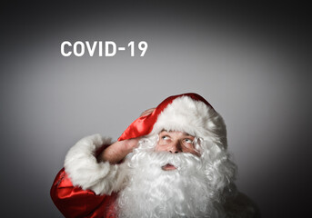 Santa Claus is looking up, he is full of doubts and hesitation. Concept about coronavirus outbreak. Text about COVID-19.