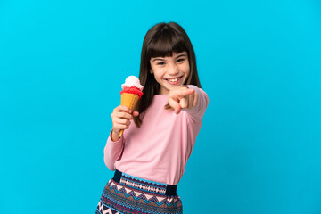 Little girl with a cornet ice cream isolated on blue background pointing front with happy expression