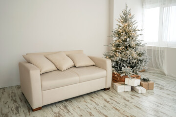 Christmas tree with presents underneath in living room, sofa. Light interior.