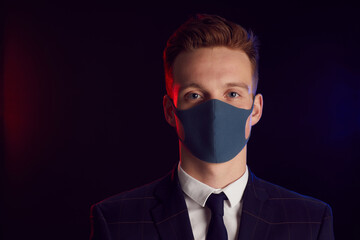 Portrait of young man wearing face mask and looking at camera while posing at party standing against black background, copy space