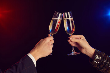 Close up of young couple clinking champagne glasses lit by party lights against black background...