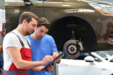 after-sales service in the car repair shop - mechanic and man talk about repairing a vehicle