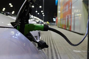 Green power supply connector in grey electric car at the parking at night. Car while charging battery. Ecological transportation. 