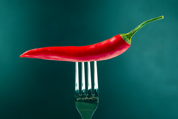 Red hot pepper with fork close-up on dark background. Healthy vegetable food and vitamins