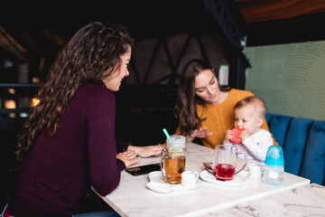 Two friends enjoying in cafe bar with cute little baby boy.