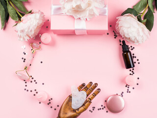 Pink background with floral peony decor, pastel gift box, beauty rose quartz stone in wooden hand. Flat lay