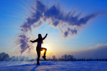 Silhouette of a sports girl at sunset in winter. Woman splashed boiling water on cold air.