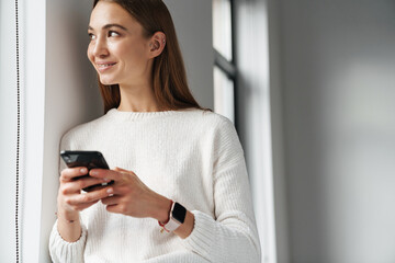 Joyful beautiful woman using mobile phone while leaning on wall