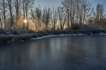 Breath of winter, first ice on the lake, dawn on a frosty morning with frost on the grass, close-up of frost, patterns on the first ice.