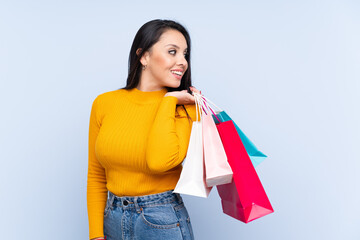 Young Colombian girl over isolated blue background holding shopping bags and looking back