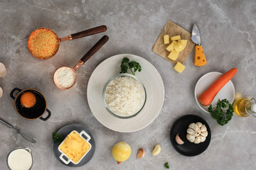 Ingredients for Making Cooking Arancini on a White Grey Marble Background. Cheese, Rice, Milk, Egg, Carrot, Parsley, Butter, Garlic, Bread Crumb, and Parmesan