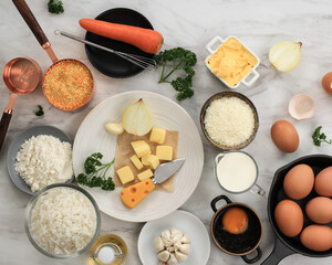 Ingredients for Making Cooking Arancini on a White Grey Marble Background. Cheese, Rice, Milk, Egg, Carrot, Parsley, Butter, Garlic, Bread Crumb, and Parmesan