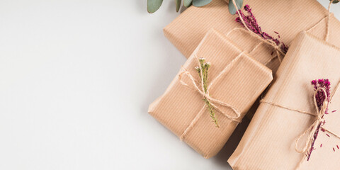 Zero waste holiday gifts wrapped in plastic free paper with dried floral decor on gray background.
