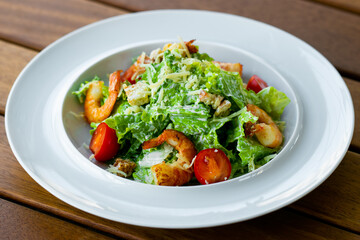 Delicious healthy caesar salad with shrimp in a white plate isolated on a wooden table.