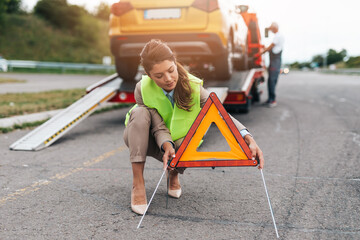 Middle age business woman after car accident putting safety or warning foldable triangle on the road. Help on the road concept.