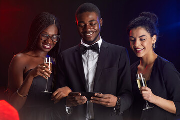 Waist up portrait of multi-ethnic group of friends looking at smartphone screen during elegant party