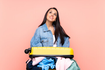 Traveler Colombian girl with a suitcase full of clothes over isolated pink background laughing and...