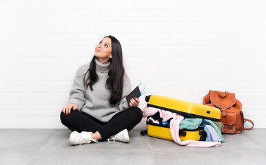 Traveler Colombian girl with a suitcase full of clothes sitting on the floor laughing and looking up