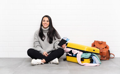 Traveler Colombian girl with a suitcase full of clothes sitting on the floor pointing back with the...