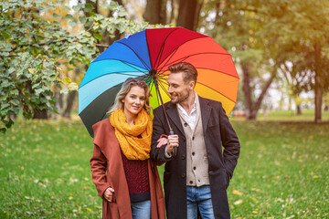 A beautiful young couple is walking in the park under a rainbow colored umbrella. A beautiful girl...