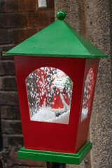 Shiny lantern Christmas decoration closeup. Toy Santa in red and green wooden retro lantern with snow globe inside