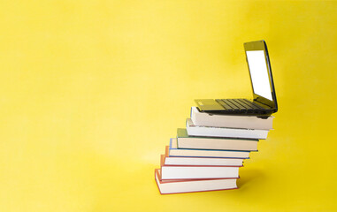 laptop and stack of books on yellow background
