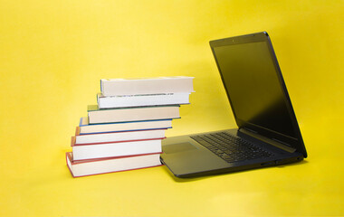 laptop and stack of books on yellow background