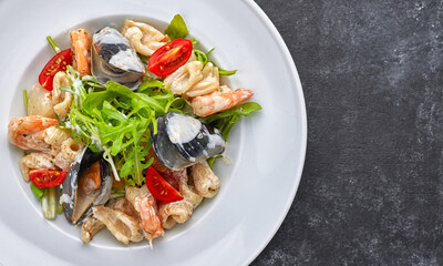 Seafood salad with mussels, squid, shrimp, on a round white plate, on a gray background