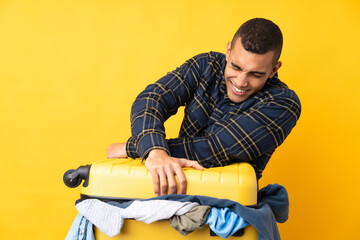 Traveler man with a suitcase full of clothes over isolated yellow background