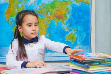 Portrait of a smart cute girl reading books on the background of the world map. The inscription on the map WORLD