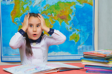 Portrait of a smart cute girl holding her head against the background of the world map. The inscription on the map WORLD