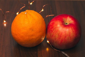 Juicy ripe red apples, orange and Christmas lights isolated on a wooden background. Making juice for Breakfast. Cooking for the holidays