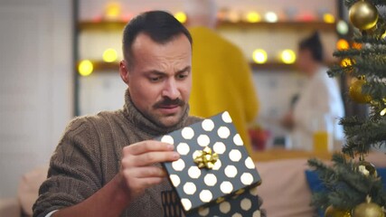 Portrait of handsome man opening Christmas present and feeling disappointed