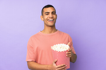 Young African American man over isolated blue background holding a big bucket of popcorns