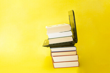 laptop and stack of books on yellow background