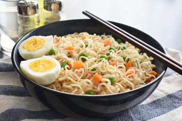 Instant noodles with vegetables (carrot and peas) and boiled egg with chopsticks. 