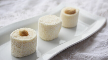 Marshmallow nougat sweets with nuts. Delicious dessert. Rolls of white nougat chocolates are served on a white plate. Selective focus.