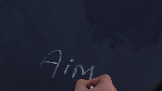 school man holding chalk writing on blackboard. aim