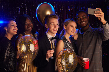 Waist up portrait of multi-ethnic group of friends taking selfie with baloons while enjoying Birthday party or prom night - obrazy, fototapety, plakaty